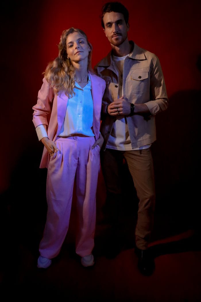 A stylish man and woman posing confidently in a studio with vivid lighting.