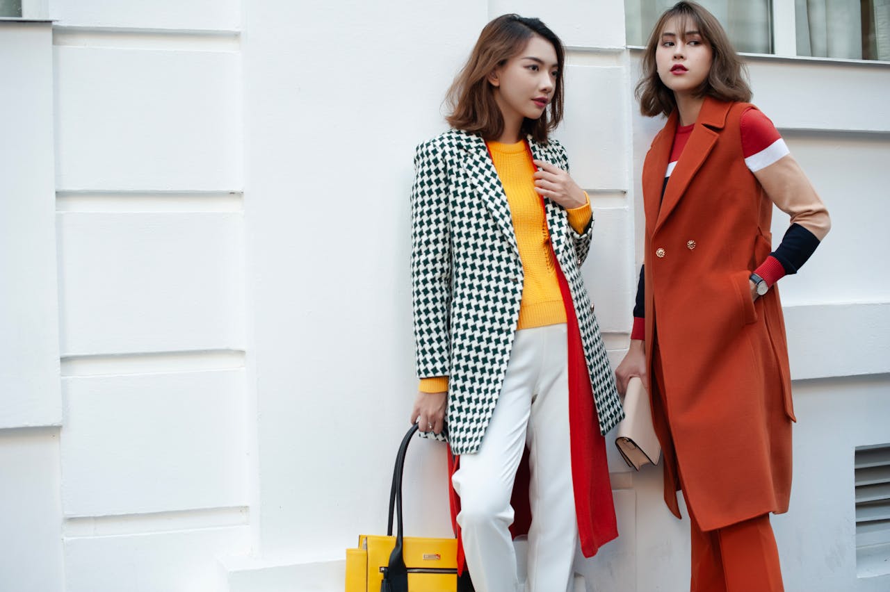 Fashionable women posing in trendy autumn outfits against a modern city backdrop.